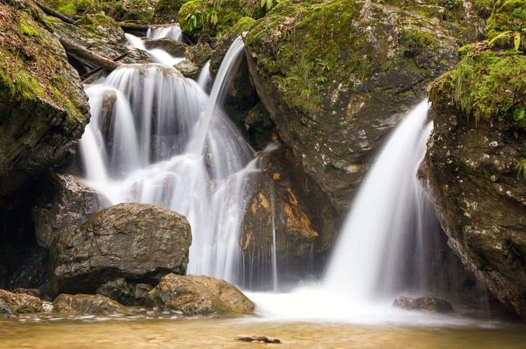 Small cascading waterfall flowing between moss-covered rocks in Pekel Gorge, Slovenia.
