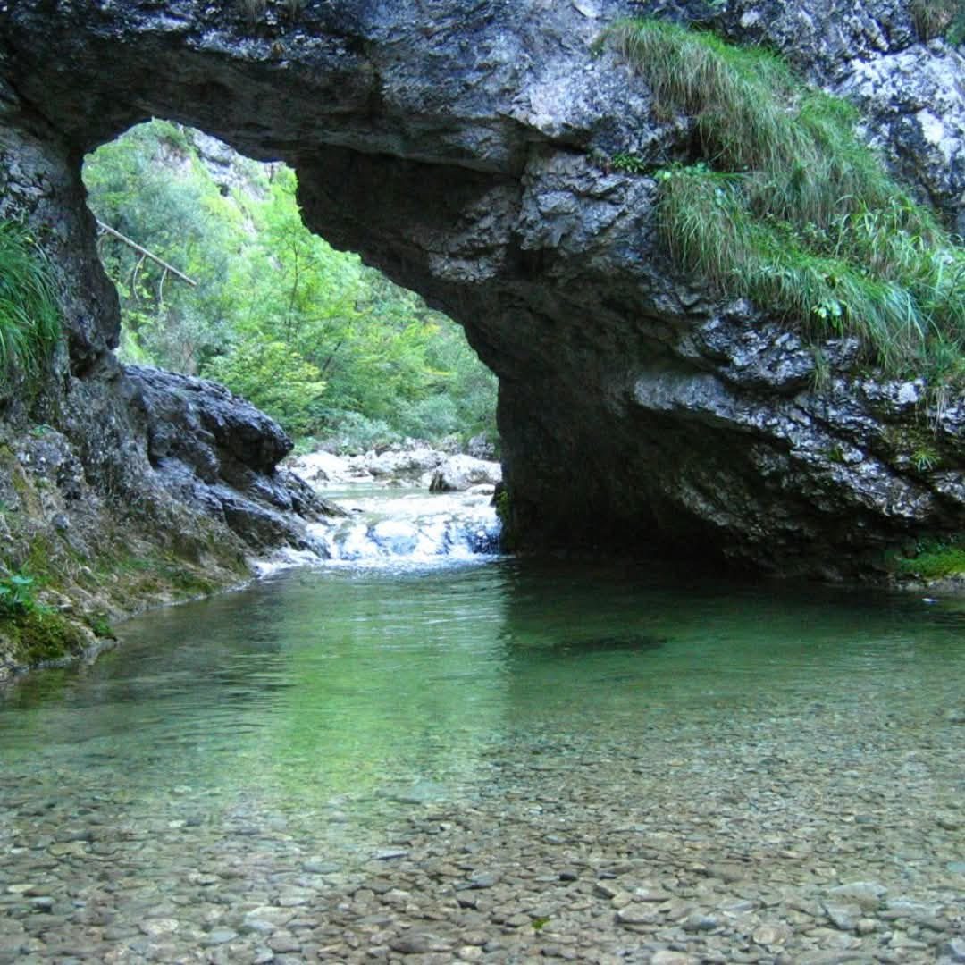 Natural rock bridge arching over the crystal clear, emerald-green water of the Iska Vintgar Gorge near Ljubljana, Slovenia.