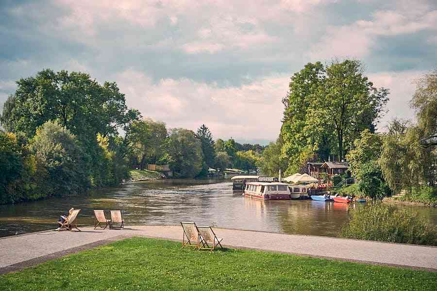 Scenic Ljubljanica River view showing leisure area with deck chairs, moored boats, and summer trees on Spica beach.