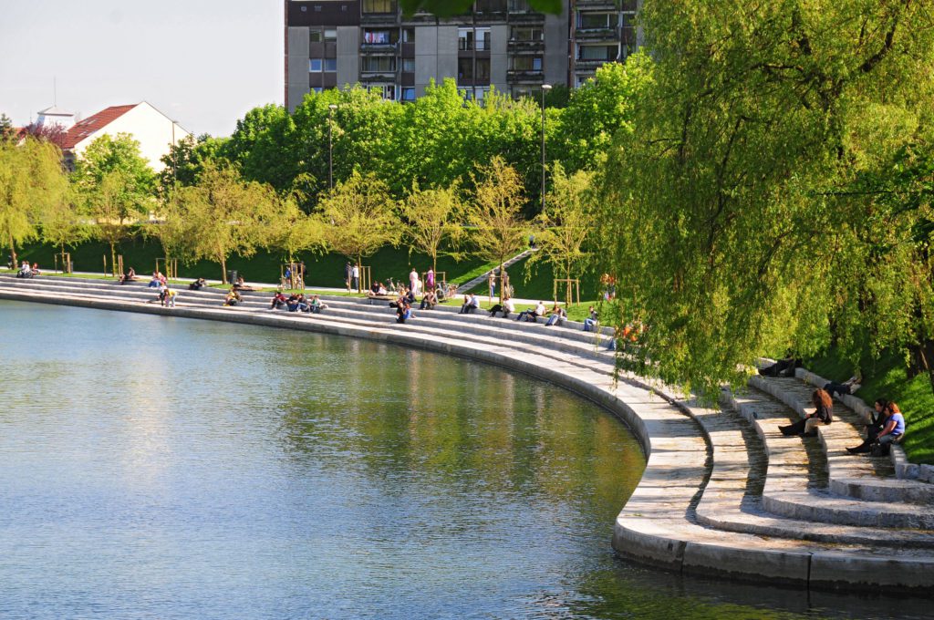Scenic view of Ljubljana River with boats, lush trees, and walking paths in Ljubljana, Slovenia.