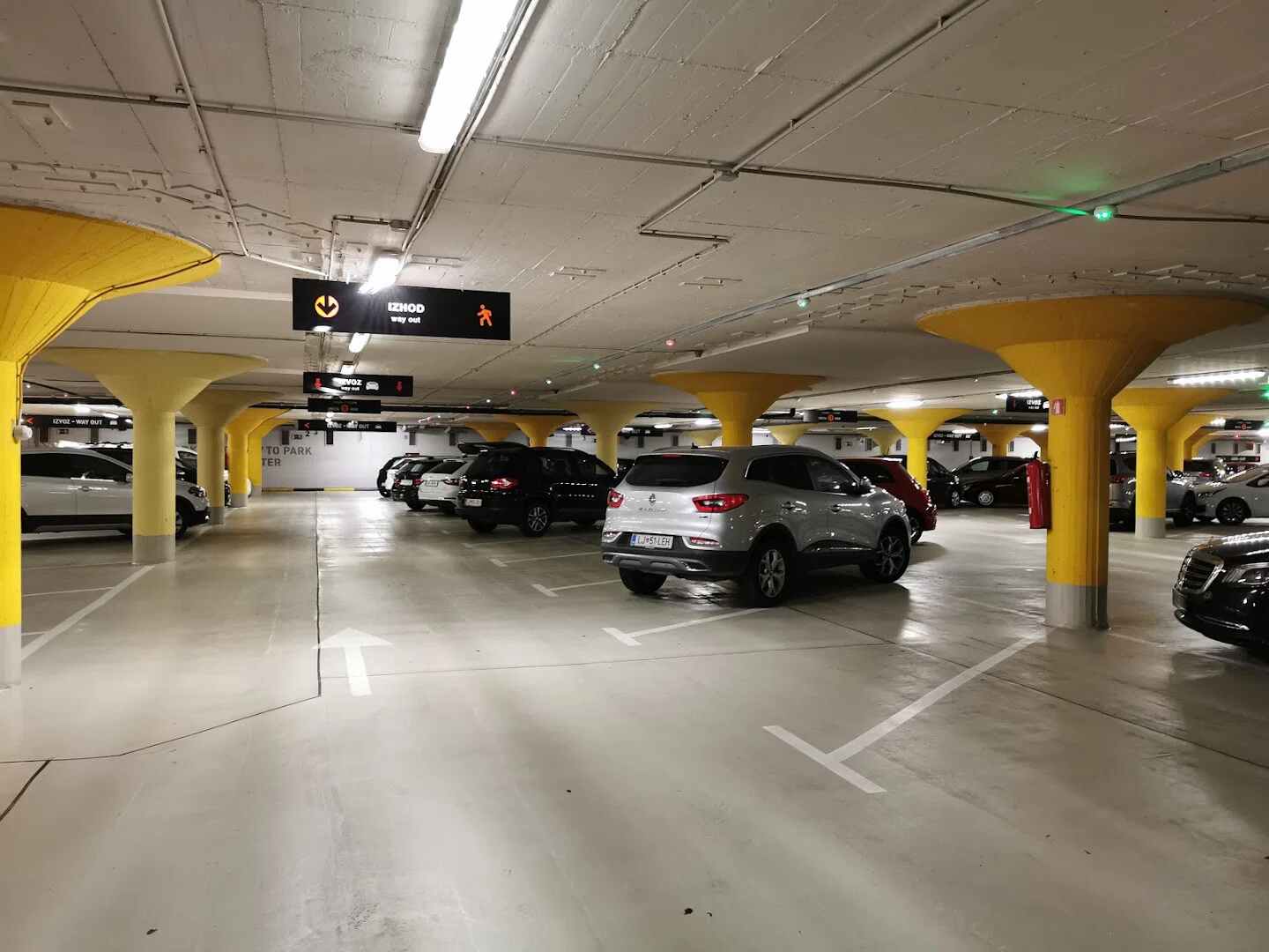 Interior view of the underground BTC parking garage (PH BTC City) featuring distinctive bright yellow pillars and parked cars in Ljubljana, Slovenia.