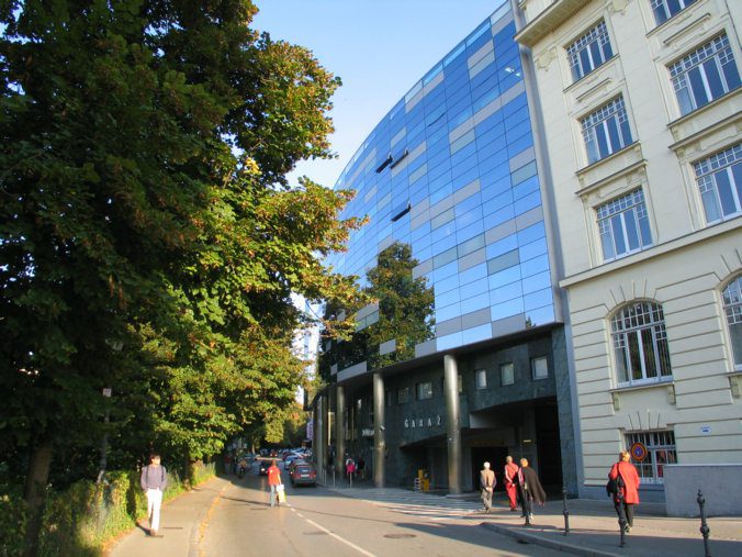 Modern glass facade of the Kapitelj parking garage (PH Kapitelj) on a street in downtown Ljubljana, Slovenia.